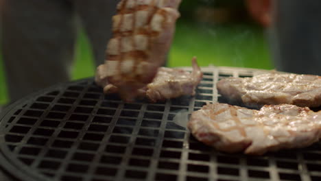 Unknown-chef-turning-around-steak-on-grate-outside.-Man-using-forceps-outdoors