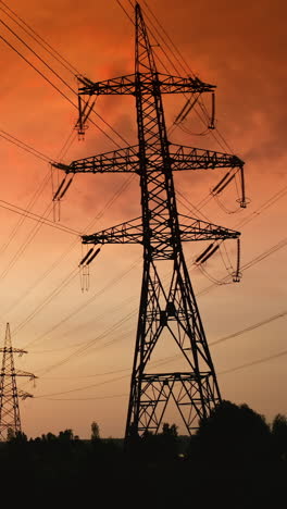 supports of high-voltage power lines against the backdrop of red sunset. sun setting and power line pylon silhouettes in epic sunset sky. vertical video