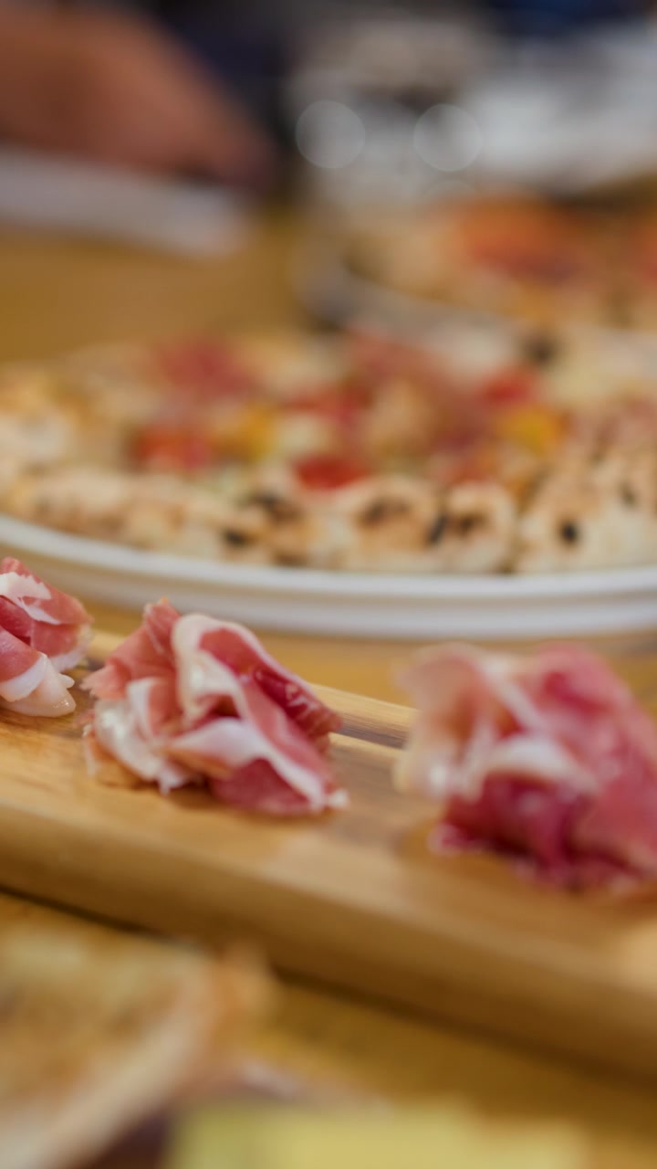 Ripresa ravvicinata in movimento di fette di prosciutto gourmet su un tagliere di legno in un ristorante.