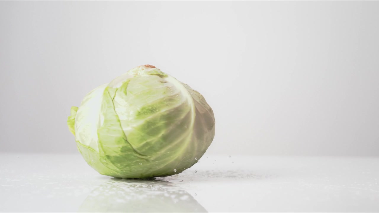 Fresh whole Green Cabbage spinning on a white backdrop in extreme slow motion 800fps high speed.