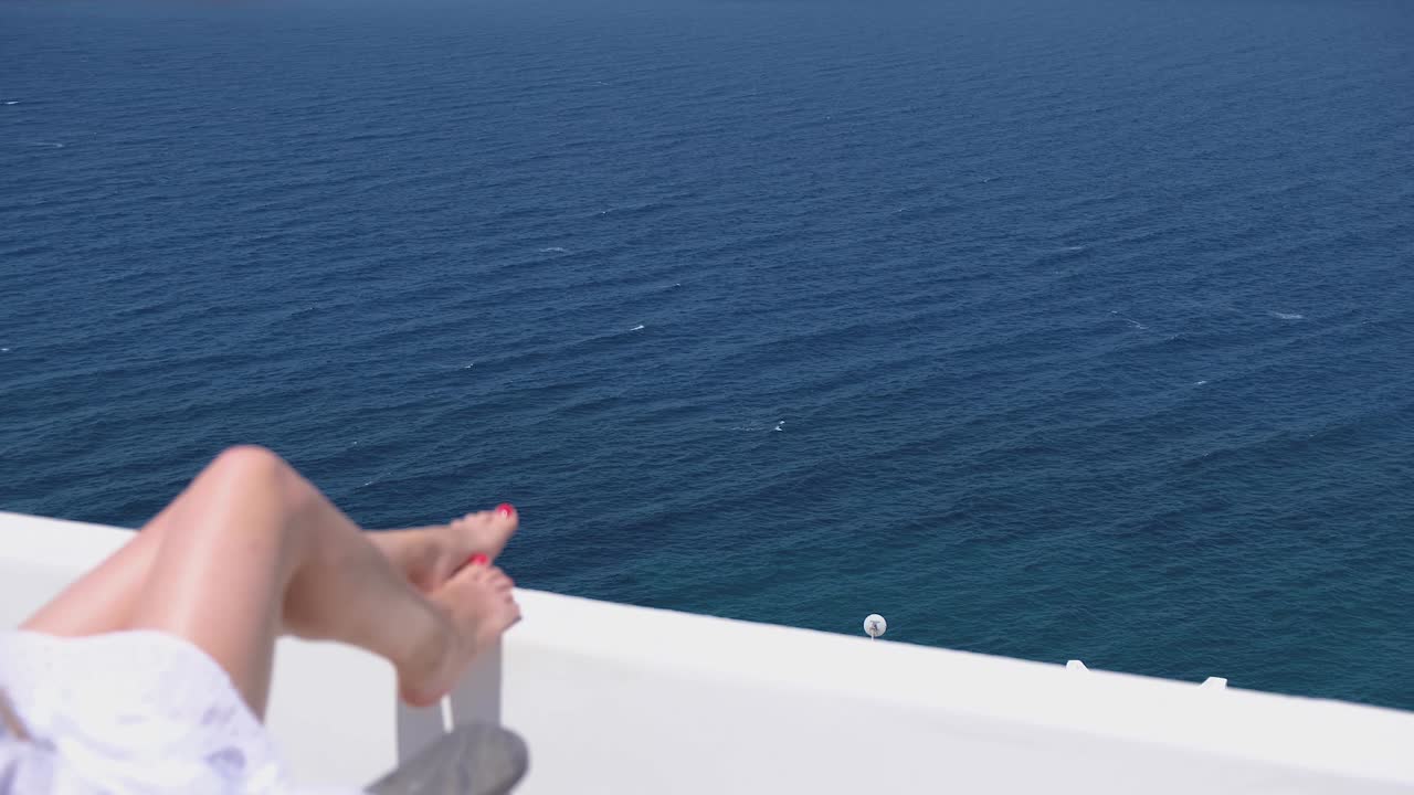 색 드레스 선글라스를 입은 여성이 바다 전망의 빌라 호텔의 테라스에 앉아 있습니다.