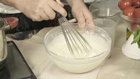 chef whipping a mixture of flour and water with hand mixer kitchen close up shot