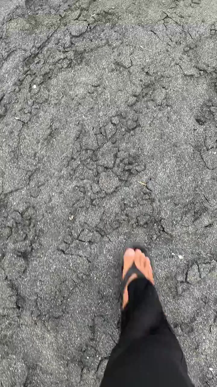 Person Walking Barefoot on Dark Volcanic Sand Beach