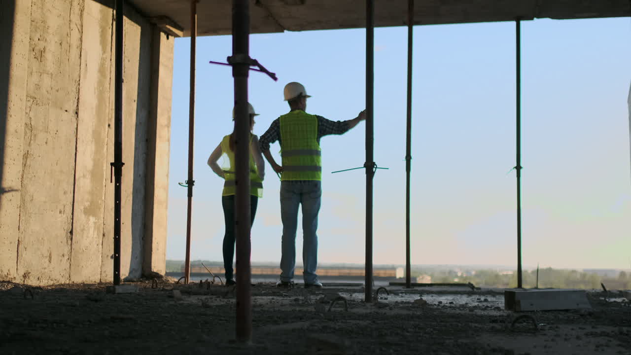 Construction Business : teamwork concept : Young engineer standing behind looking at a building site wearing a safety helmet