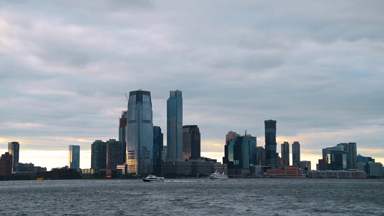 New York, USA, 26 maggio 2026: Skyline di Jersey City attraverso il fiume Hudson al crepuscolo. Torri e traghetti in silhouette sotto nuvole drammatiche e coperte con luce calante.