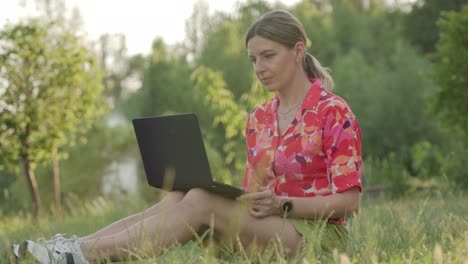 una mujer de mediana edad trabaja usando su portátil en un parque público. ella escribe y piensa.