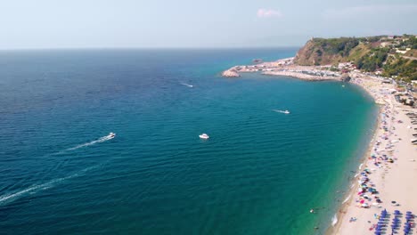 aerial, drone shot of boats on the coast of calabria, at the palmi beach, on a sunny day, southern italy