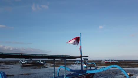 national flag of indonesia waves in the wind at boats seascape, sanur bali beach