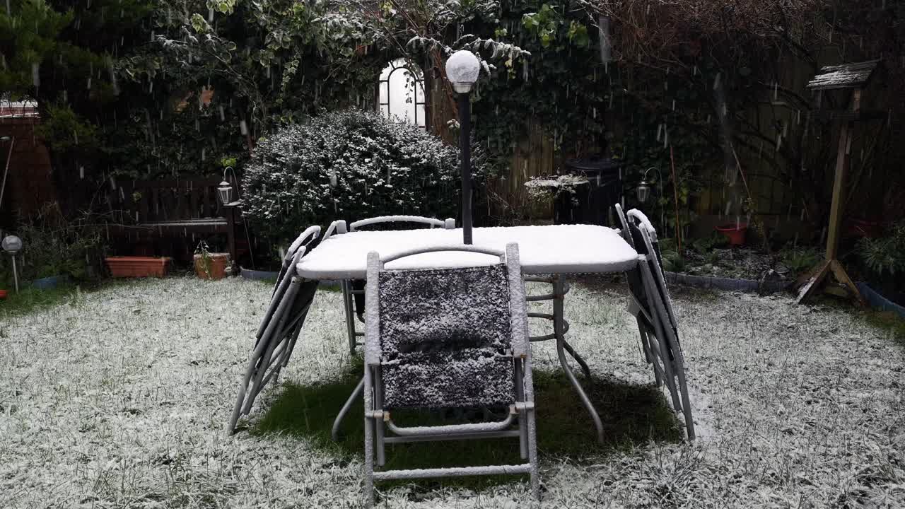 pesados copos de nieve de invierno cayendo sobre mesas y sillas de jardín en desuso en una fría residencia suburbana