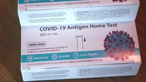 covid 19 at home antigen test kit for coronavirus 3 white and blue boxes of tests stacked up close wide shot focusing on bottom box and slowly twisting