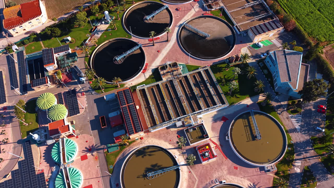 Aerial top view of industrial wastewater treatment plant facility. Top down view of circular sedimentation tanks, solar panels, and industrial buildings at a water processing plant