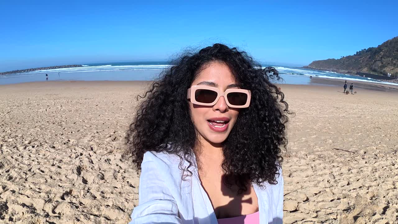 Người phụ nữ trẻ đang quay vlog và trò chuyện trên bãi biển đầy nắng.