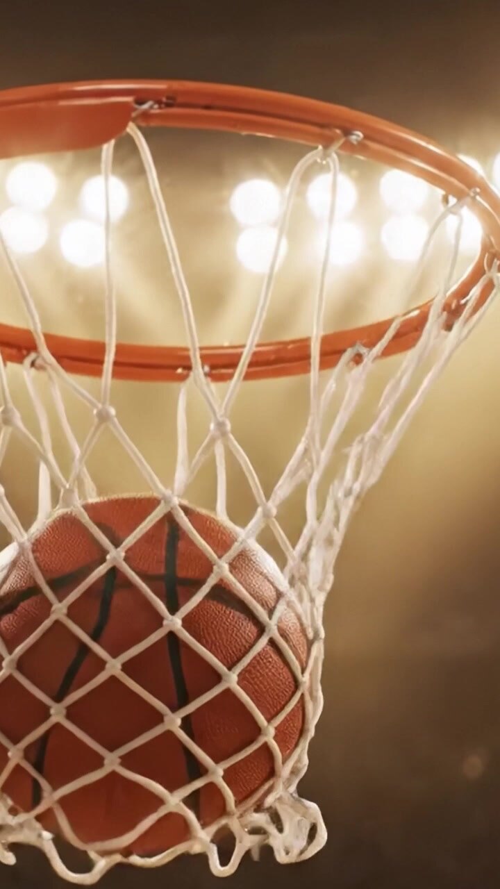 Una emocionante exhibición de un momento de baloncesto, capturando la intensidad del juego con el balón elevándose hacia la canasta bajo las brillantes luces del estadio.