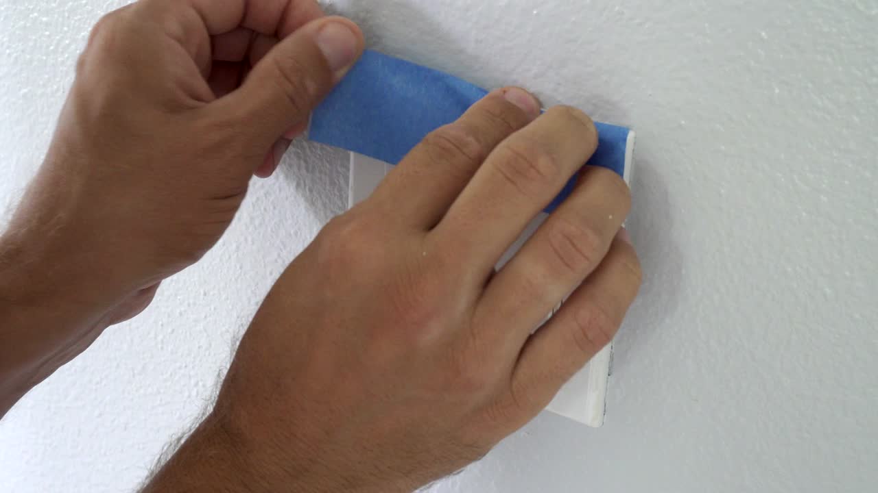4k, pintor usando cinta azul de enmascaramiento para asegurar el interruptor de luz. preparación para la pintura de la habitación.