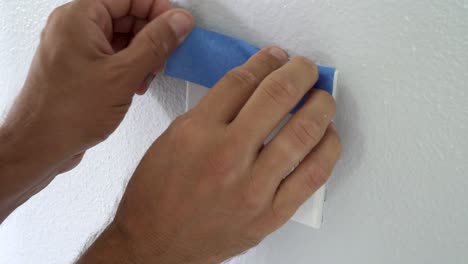 4k, painter using masking blue tape to secure light switch. preparation for room painting.