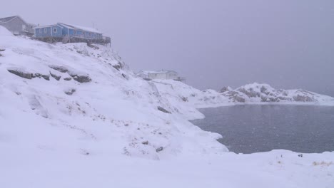 그린란드 일루리사트의 눈보라 속에서 눈 덮인 북극 언덕 해안에 있는 두 집의 슬로우 모션 비디오