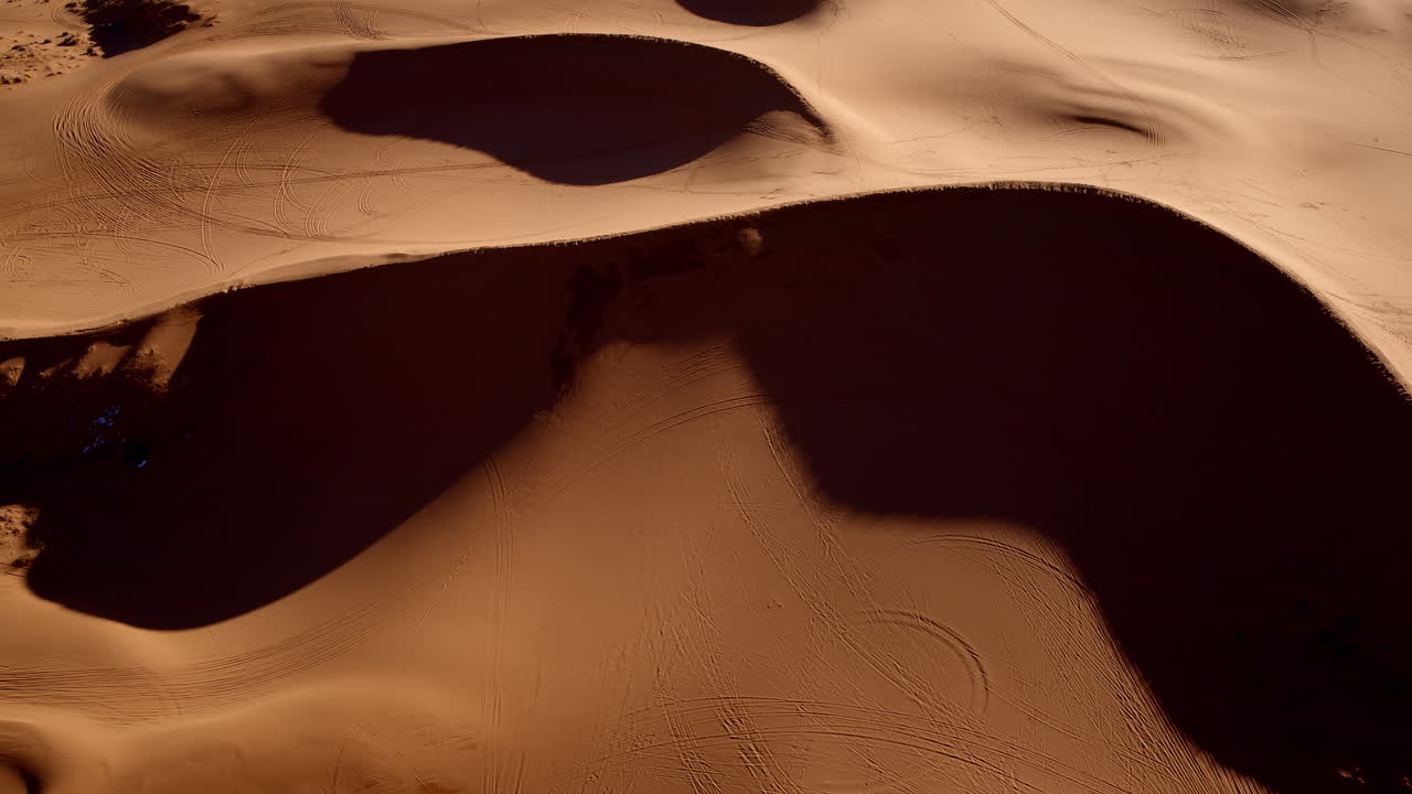 Sweeping drone footage showcases the colorful pink sand dunes and unique terrain.