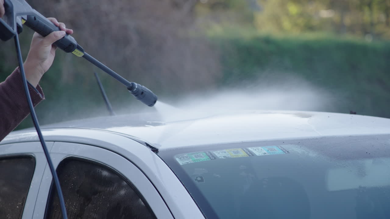 Personne lavant une voiture blanche avec un nettoyeur haute pression.