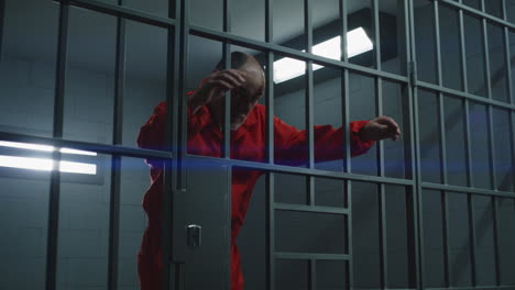 close up of prisoner in orange uniform holding metal bars in prison cell          (stock footage)