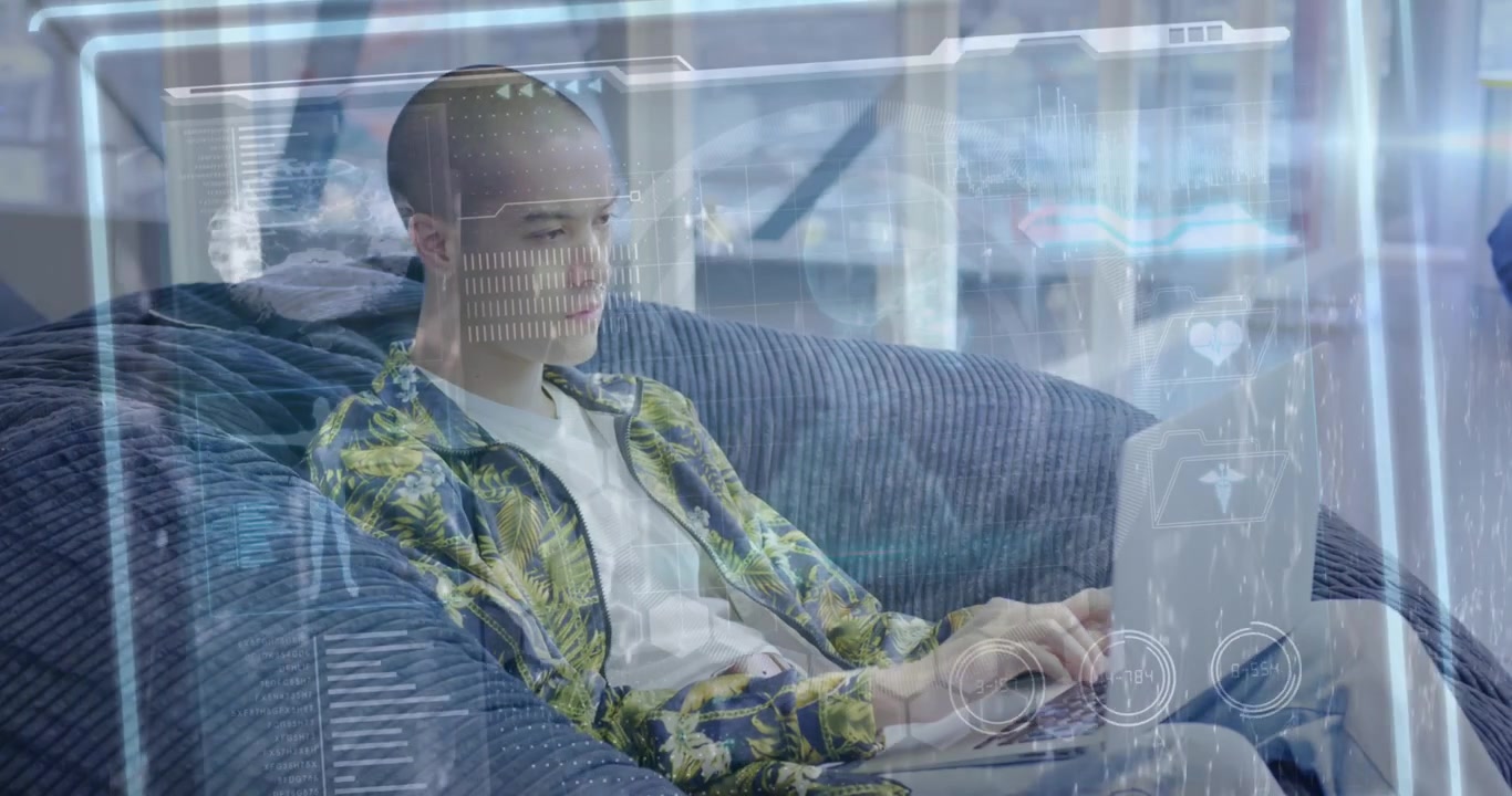 En ung mand sidder i en sækkestol og bruger en bærbar computer på et moderne åbent kontor