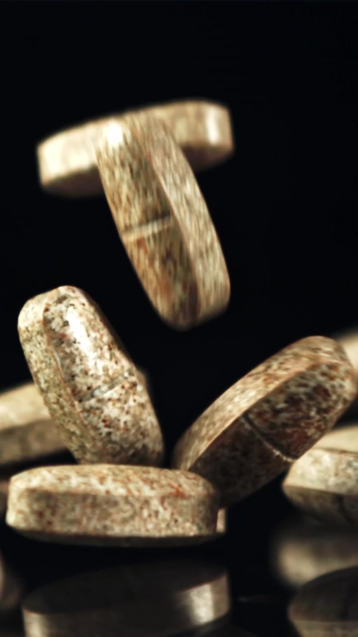 Brown Tablets Falling in Slow Motion on Black Reflective Surface