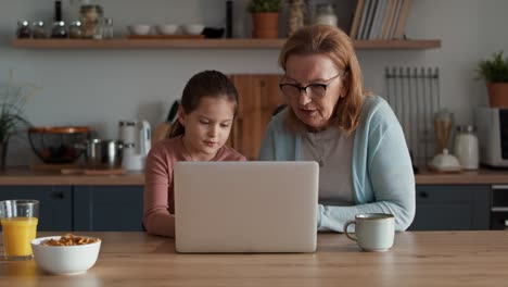 abuela y nieta caucásicas usando una computadora portátil en la cocina