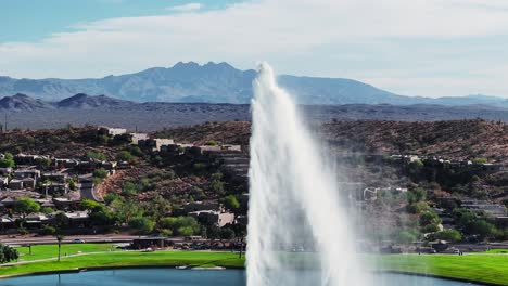 Water-spurts-up-into-air-arching-back-down-with-epic-view-of-desert-southwest-mountains,-Fountain-Hills-Arizona-aerial