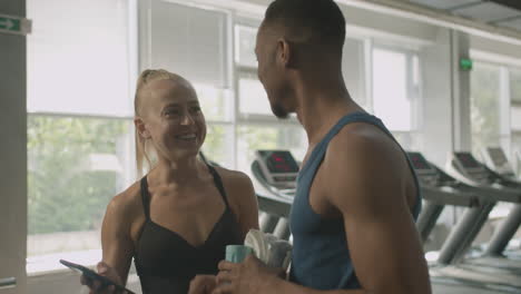 close-up view of caucasian female monitor and an athletic african american man talking in the gym.