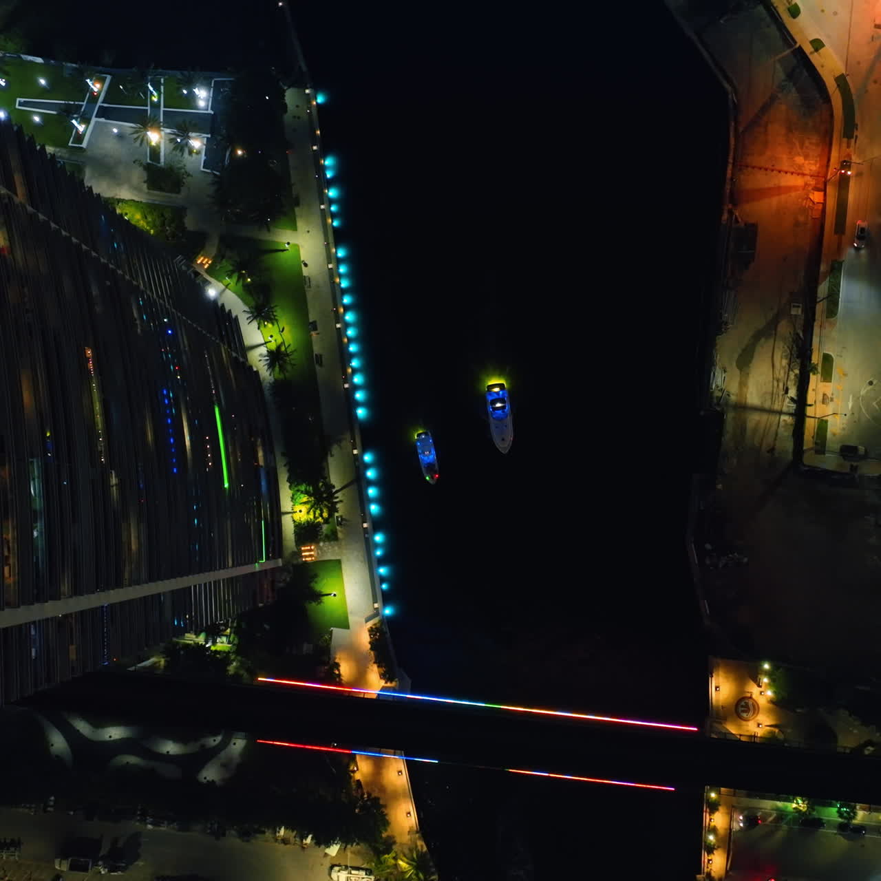 Two highlighted boats sailing slowly by the dark river. Top view of Miami River at night.