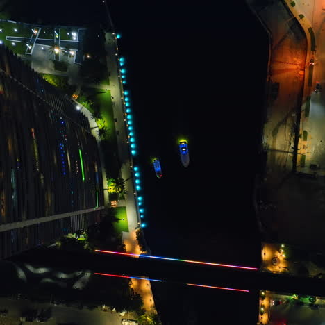 two highlighted boats sailing slowly by the dark river. top view of miami river at night.