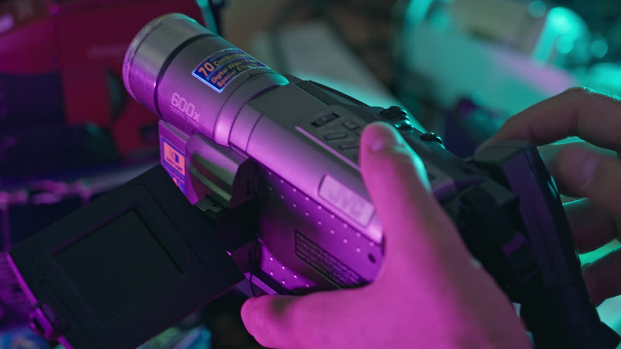 Mani che azionano una videocamera JVC d'epoca con luci al neon