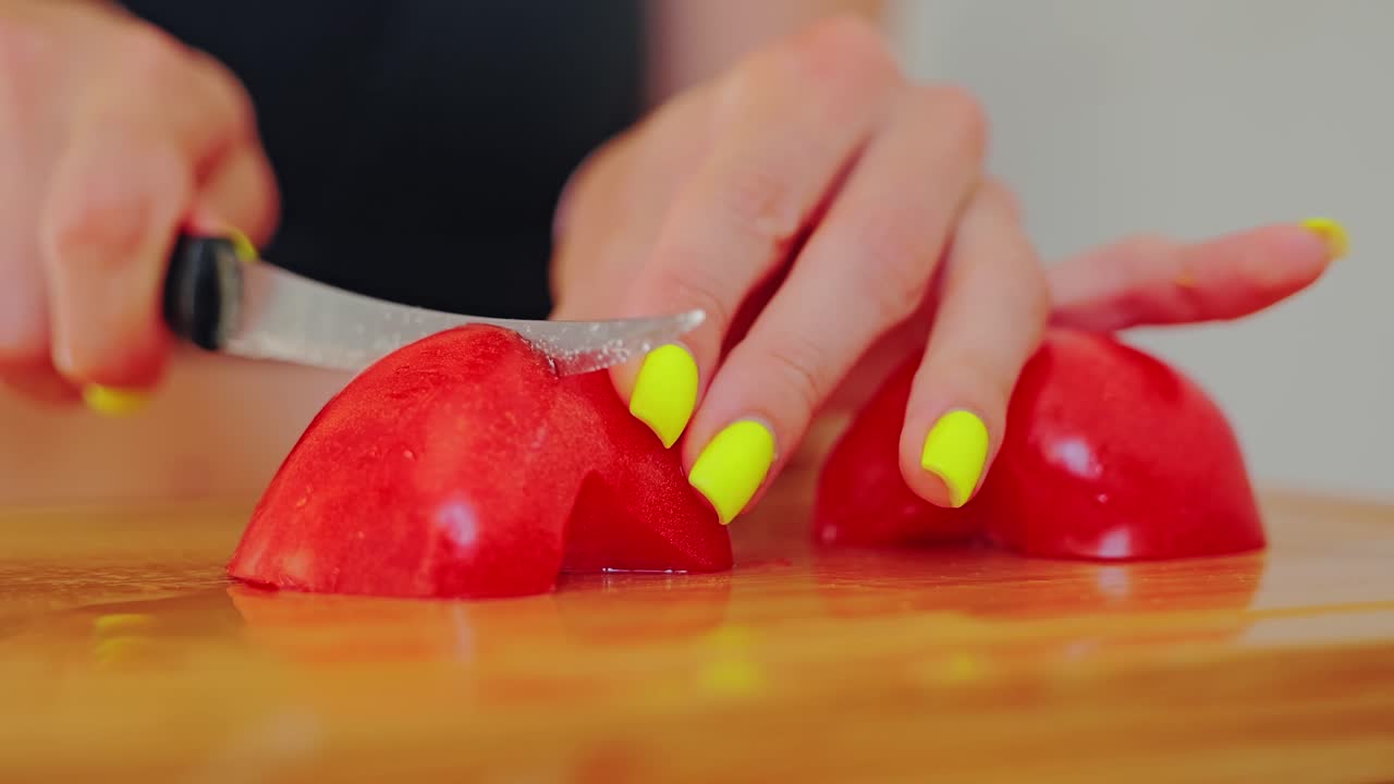 Close up of female hands cutting ripe red tomato with bright yellow manicure