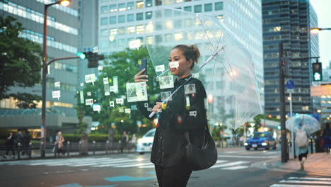 Woman-stands-in-city-street-holding-transparent-umbrella-looking-at-smartphone