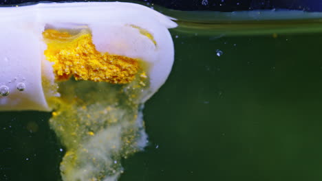 pill dissolving in water, releasing powder and bubbles as it dissolves.
