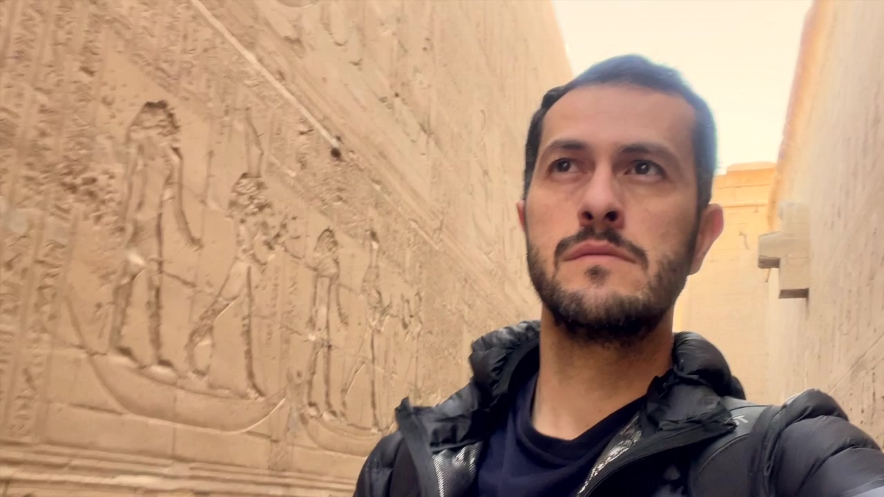 ARKEOLOG BERJALAN DAN MENJELAJAHI HIROGLIF MESIR DI ANTARA DINDING DI DALAM KUIL HORUS DI EDFU MESIR. Arkeologi Afrika. Egiptolog, Egiptologi. PENJELAJAH WISATAWAN DENGAN TAS. PERJALANAN WANDERLUST