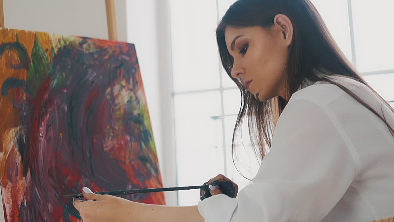 Woman artist looks at brush sitting near drawing on easel