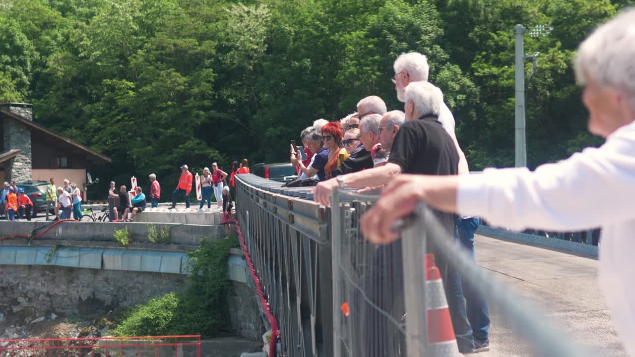 People gather on a bridge watching construction rigging in Tende, France on a sunny day