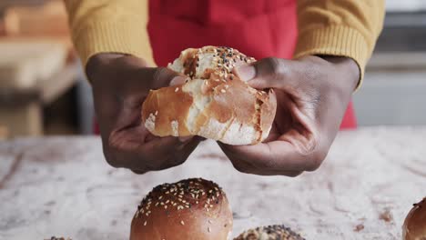 midsection of african american male baker working in bakery kitchen, ripping roll, slow motion