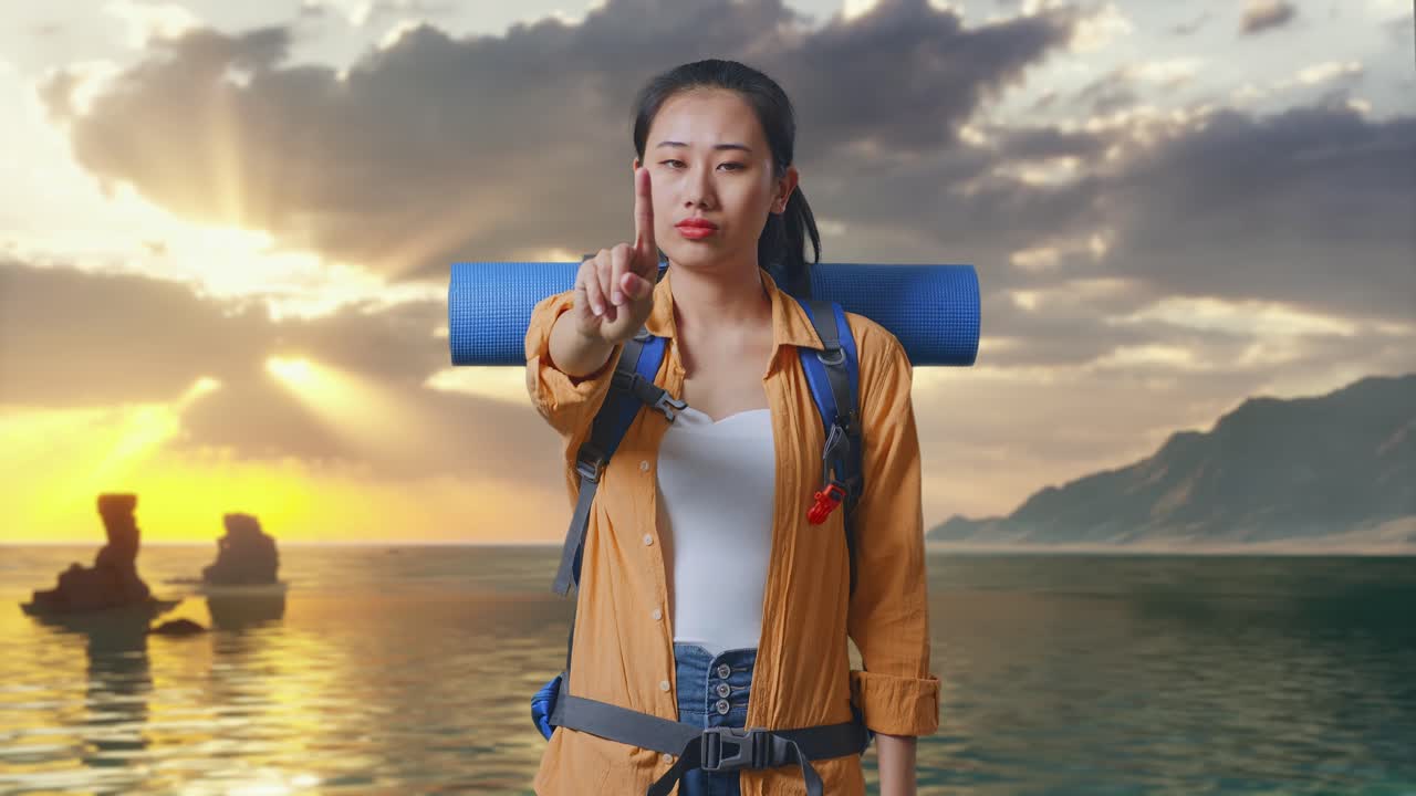 Nữ du khách đi bộ đường dài người châu Á đeo ba lô leo núi, không có cử chỉ ngón trỏ khi đứng trên bãi biển lúc hoàng hôn