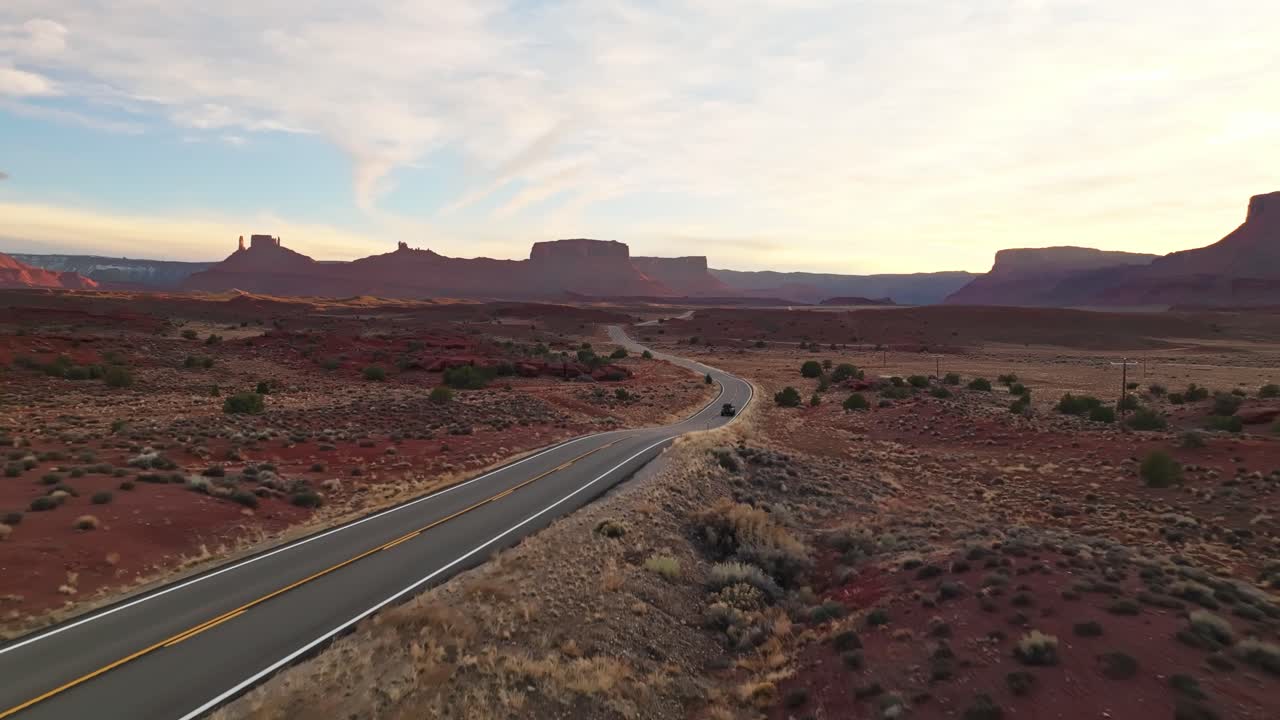Wide view of golden hour sun lighting red desert cliffs and winding road across barren landscape, Moab Utah USA