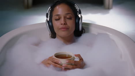 woman relaxing in a bubble bath with headphones and tea