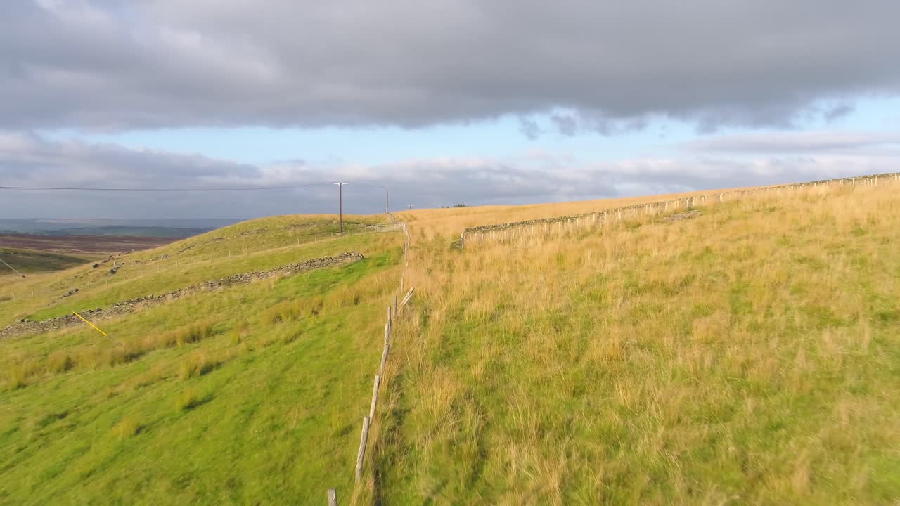 Drone footage following the path of a farmer's fence over fields and moorland in West Yorkshire, UK, England at golden hour in the evening