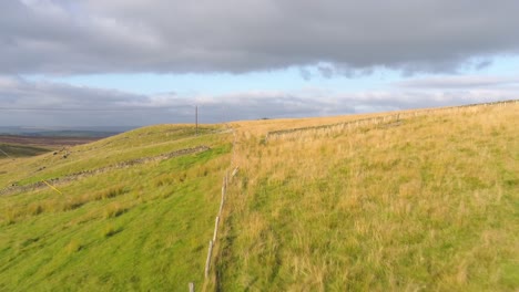 drone footage following the path of a farmer's fence over fields and moorland in west yorkshire, uk, england at golden hour in the evening