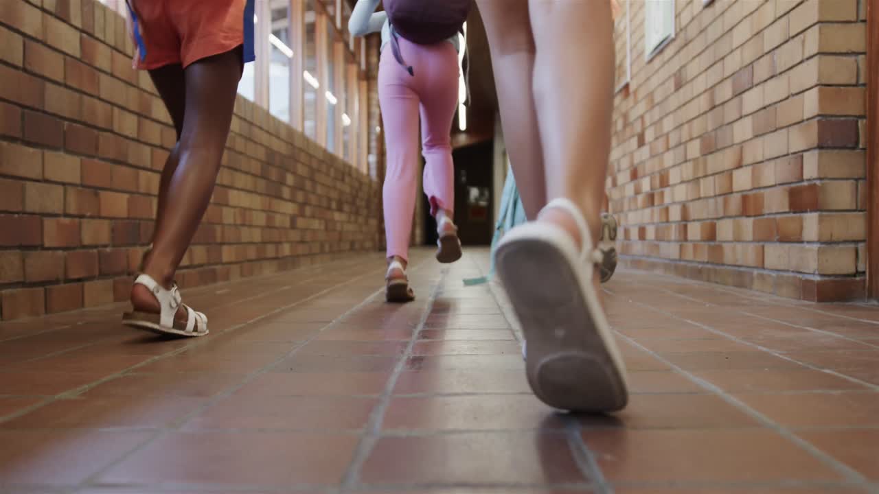 Niñas diversas con mochilas escolares corriendo por el pasillo de la escuela primaria en cámara lenta.