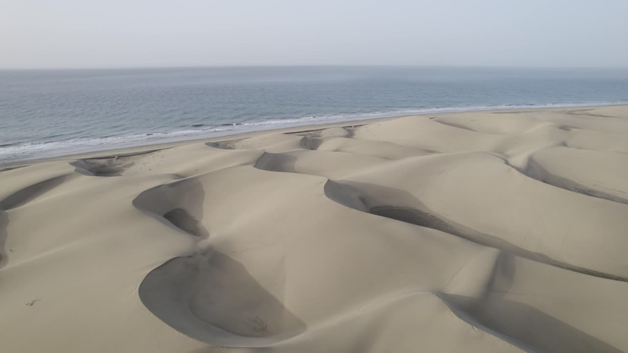 Circular drone footage of coastline with dune sand and green ocean water on the island of Gran Canaria