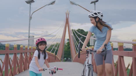 mother and daughter cycling on a bridge