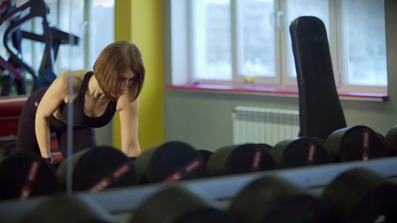 Žena cvičí s činkami v posilovně