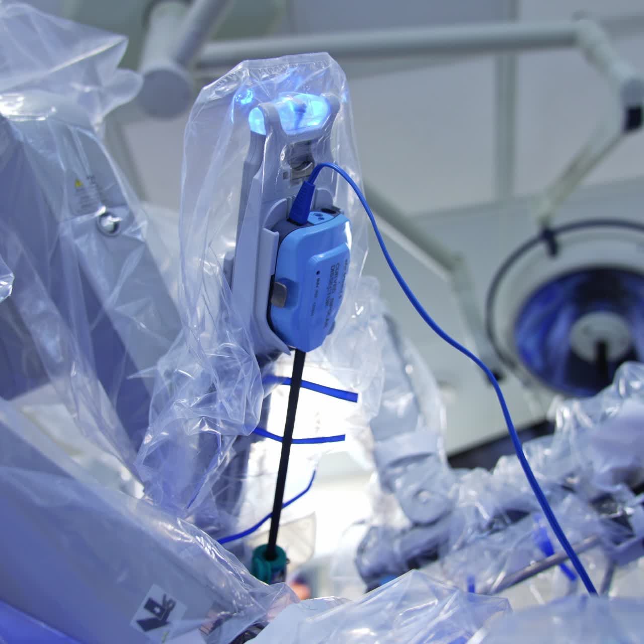 Da Vinci robot working in the modern surgery room. Robotic arms covered with plastic moving slowly when the light in the room is switched off