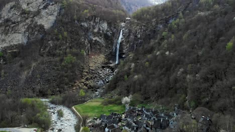 aerial flyover over the rooftops of the old stone houses of the village of foroglio in ticino, switzerland towards the waterfall at dusk