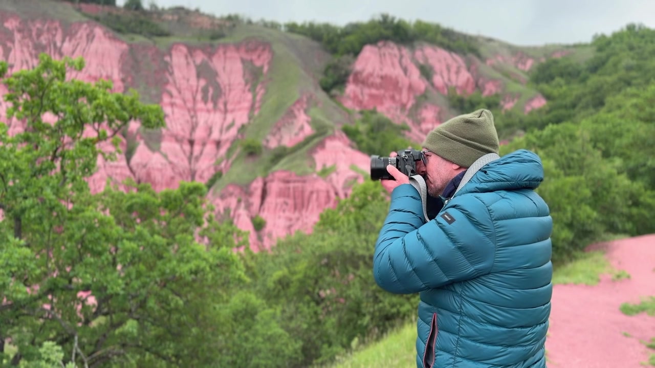 Moden mandlig fotograf med et kamera tager billeder af de unikke røde klippeformationer ved Rapa Rosie, et geologisk monument i Rumænien.